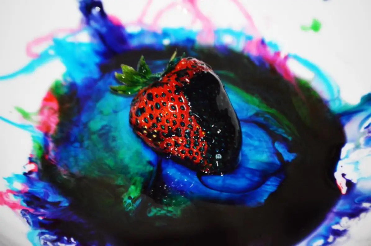 A strawberry in marbled pools of corn syrup, water, and food coloring on white printer paper